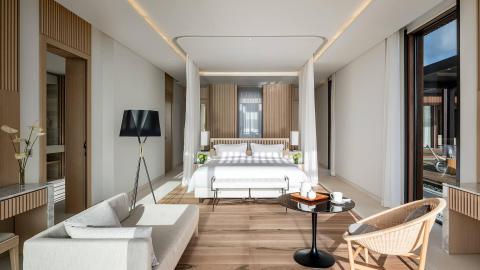 Elegant modern bedroom with king-size bed, natural light, and cozy seating area.