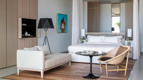Modern bedroom with white bed, black lamp, beige chaise lounge, and greenery view