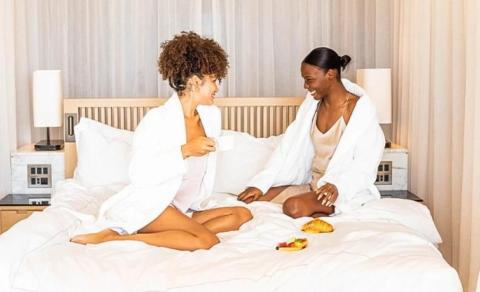 Two women in bathrobes enjoying a chat with breakfast in a cozy hotel room.