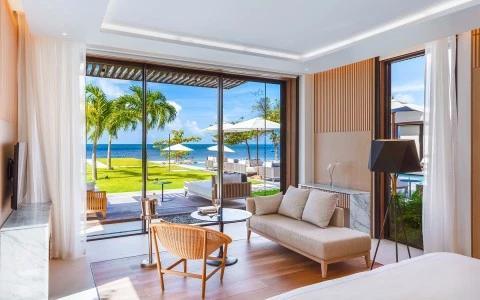 Elegant beachfront room with beige couch, chair, and garden view for serene living.