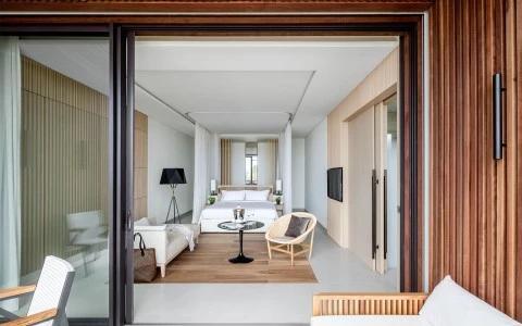 Modern hotel room viewed from balcony with minimalist decor and neutral tones.