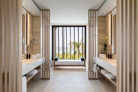Modern tropical resort bathroom with dual sinks, mirrors, and beach view.