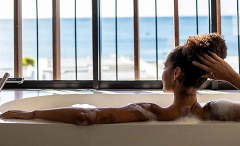 Person relaxing in a bubble bath with ocean view tattoo visible