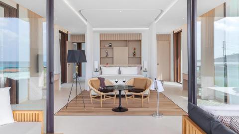 Modern bedroom with sea view, white linens, and stylish wooden furniture.