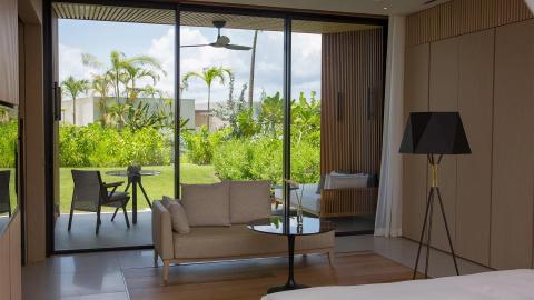 Modern room with glass doors opening to a lush garden, merging indoor and outdoor spaces.