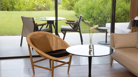 Modern indoor space with glass doors, wicker chair, minimalist sofa, and garden view.