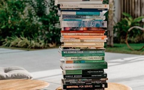 Stack of books on wooden table in a serene garden setting with chair