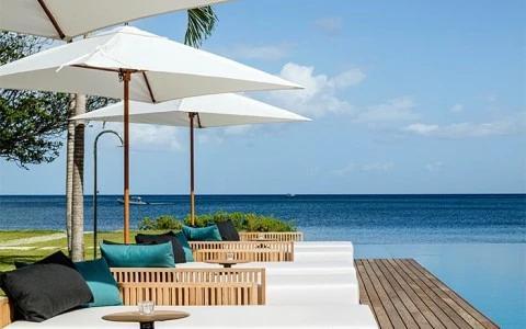 Modern outdoor seating by the ocean with green and blue cushions under a white umbrella
