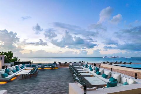 Upscale outdoor lounge with ocean view, sofas, and dining set on wooden deck.