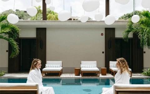 Two women chatting by a modern pool surrounded by plants and lights.