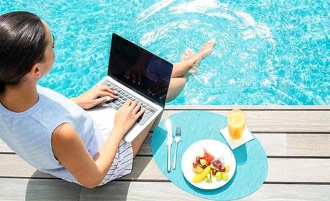 Woman using laptop by pool with fruits and juice on table, serene work setting