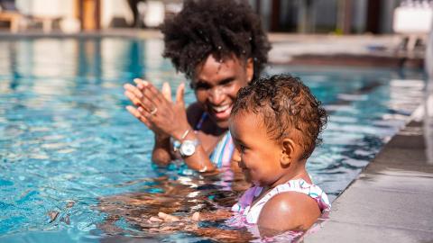 Adult playing with child in pool, sunny day backdrop, joyful moment.