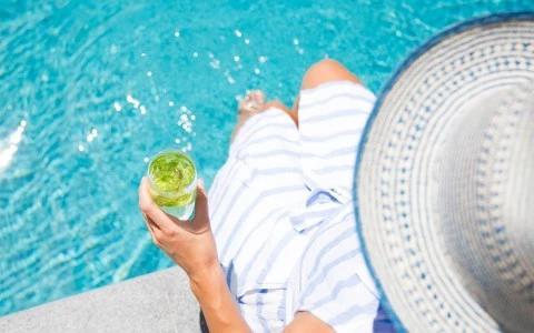 Person in striped cover-up enjoying a mojito by the pool on a sunny day