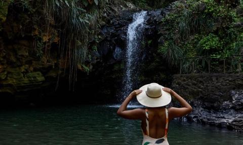 Person in white hat admires secluded waterfall in lush setting