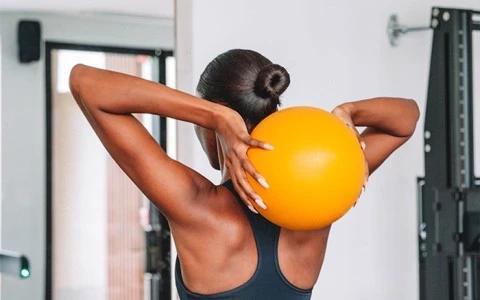 Woman in gym with bun stretching using orange exercise ball
