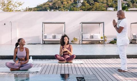 Adults practicing yoga by poolside against a backdrop of green hills