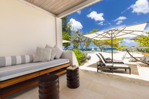 Relaxing resort beach area with cushioned bench, umbrella, and ocean views.
