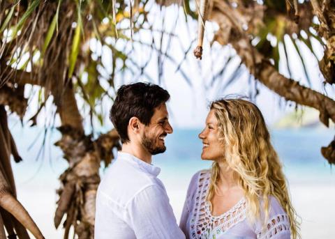 Couple smiling under tree at beachfront, evoking warmth and intimacy