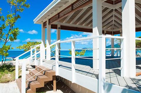 White beachside gazebo with benches under clear blue skies, perfect for relaxation.