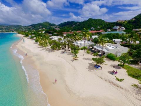 Aerial view of a beach with crystal clear waters, white sands, and lush green hills.