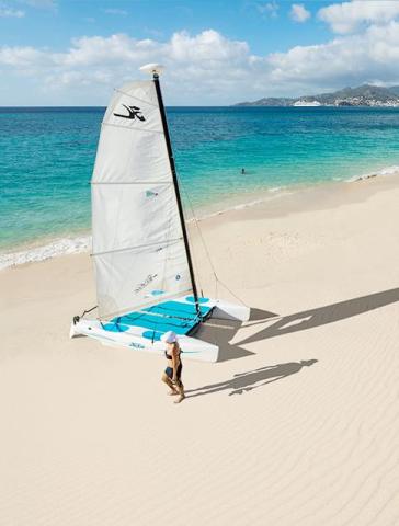 Sandy beach and blue sea with person by sailboat under clear sky