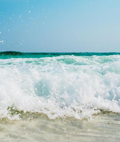 Turquoise ocean waves breaking near shore with sunlight and clear blue sky.