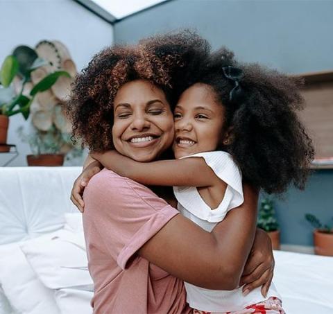 Joyful embrace between woman in pink top and girl in white shirt outdoors.