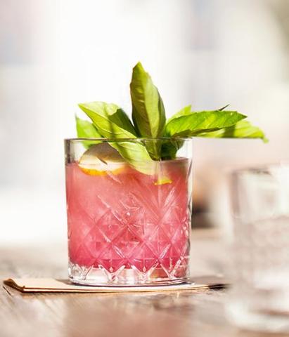 Colorful pink fruit-flavored drink with basil and lemon in a casual setting.