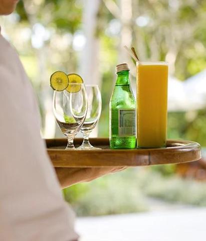 Person holding tray with drinks and bottles in a green outdoor setting