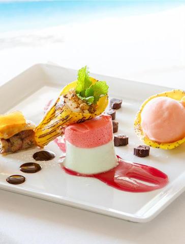 Elegant dessert with mousse cake, sliced fruit, nuts, sorbet, and chocolate on white plate