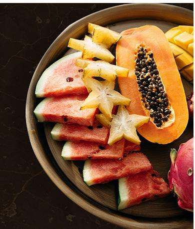 Assorted tropical fruits on a plate including watermelon, star fruit, mango, papaya, dragon fruit.