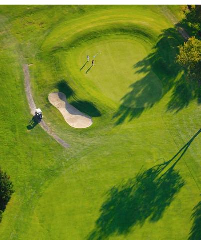 Aerial view of golf green with golfers, sand bunker, and cart in morning light.
