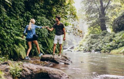 Man helping woman cross stream during forest hike