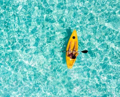 Person kayaking in turquoise water with sandy bottom, aerial view
