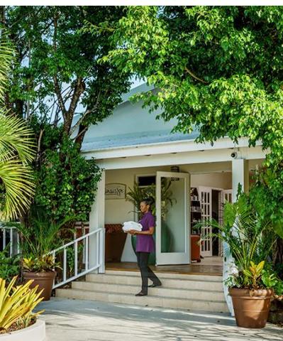 Person exiting white building with greenery, carrying tray on sunny day.