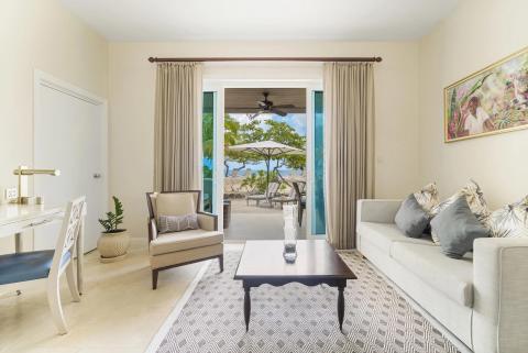Beachfront room interior with desk, sofa, and view of sandy beach and sea