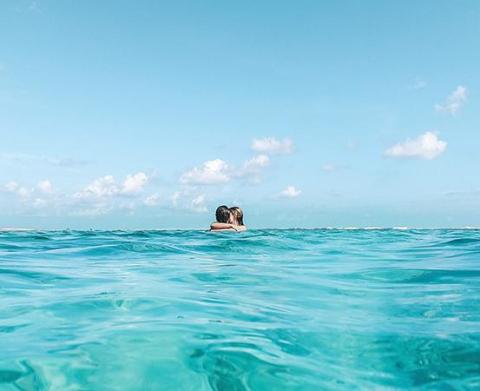 Two people floating in a turquoise ocean under a clear sky with clouds