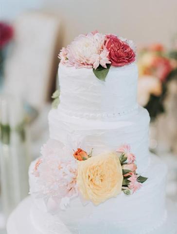 Elegant three-tiered wedding cake decorated with pink and yellow flowers