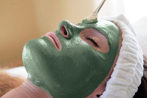 Person relaxing with green facial mask in a serene spa setting