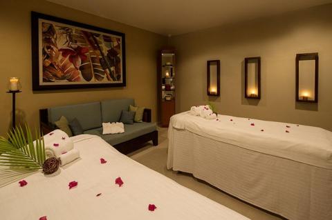 Spa room with beds, rose petals, green sofa, and botanical painting for relaxation.