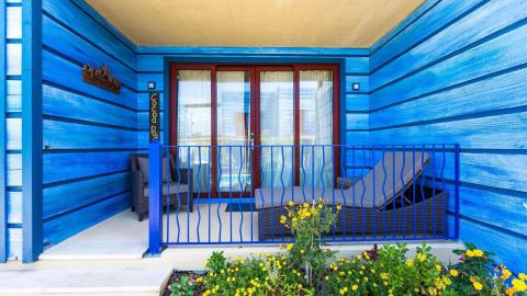 Colorful house exterior with blue siding, red framed doors, and a cozy porch seating area.