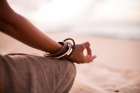 Person with bracelets sits by the beach at sunset, relaxed and meditative