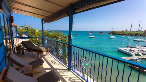 View from blue balcony over turquoise sea with boats and comfy lounge furniture