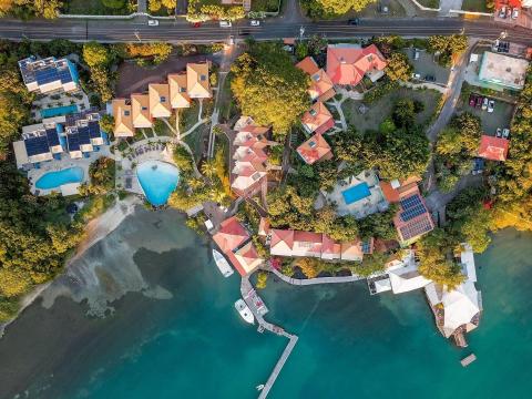 Aerial view of coastal resort with orange rooftops, pools, docks, and boats by the sea.