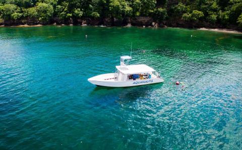 AQUANAUTS boat on turquoise water with swimmers, tropical setting