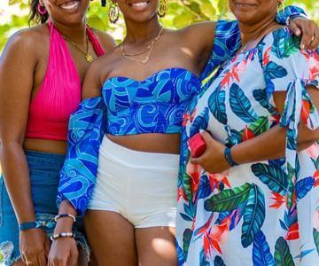 Three joyful women in colorful outfits smiling outdoors at a social event.