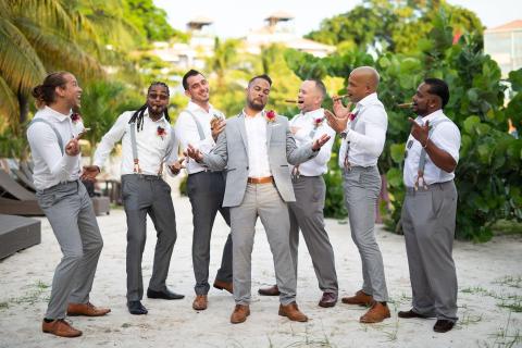 Group of seven men in semi-formal attire laughing outdoors at a tropical venue