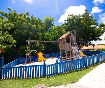 Colorful playground with wood structure, slide, swings, and lush trees in background