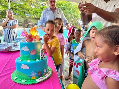 Outdoor kids birthday party with cartoon pig cake, swimwear, adults, and festive joy