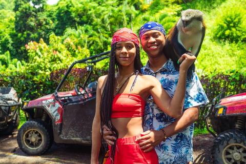Couple with monkey on safari trip by ATV in lush greenery